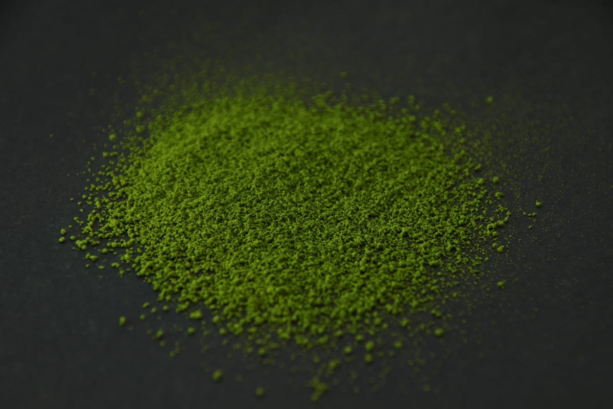 Bright green SR-8 matcha powder heaped on a dark surface