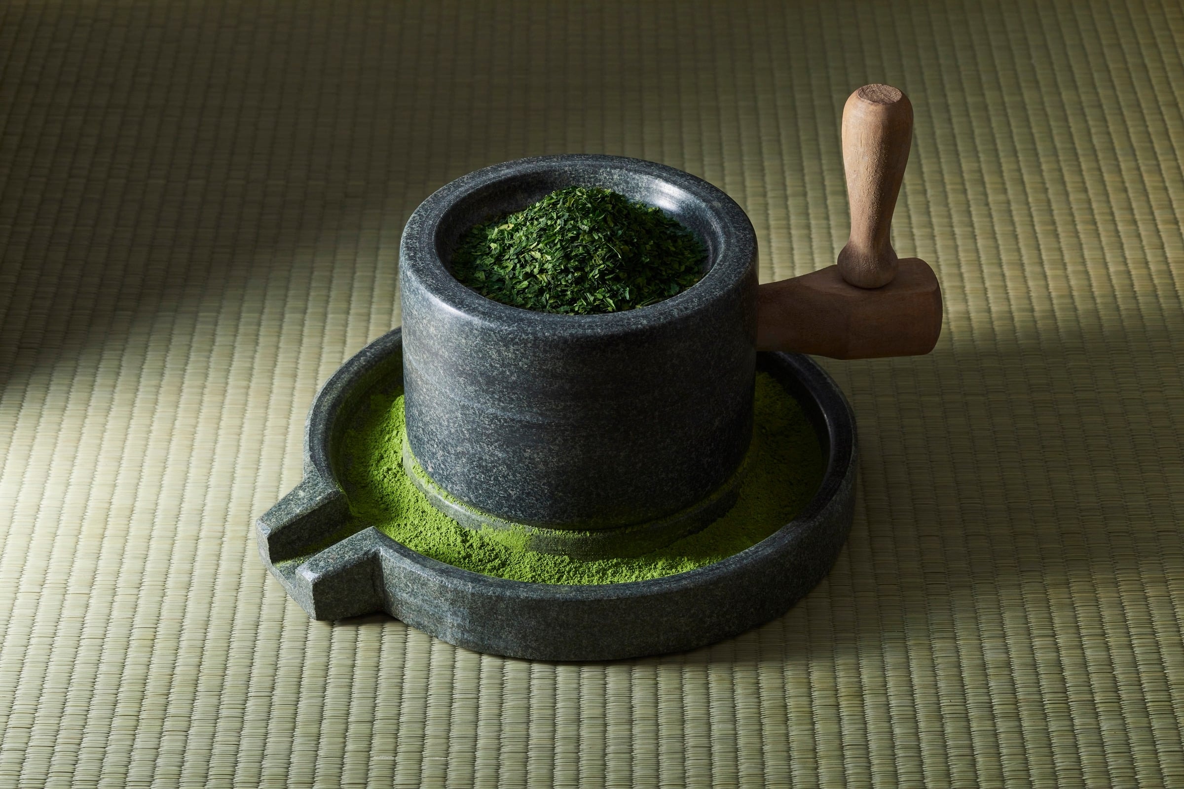 A granite stone mill with tencha leaves on top and fresh matcha around its base