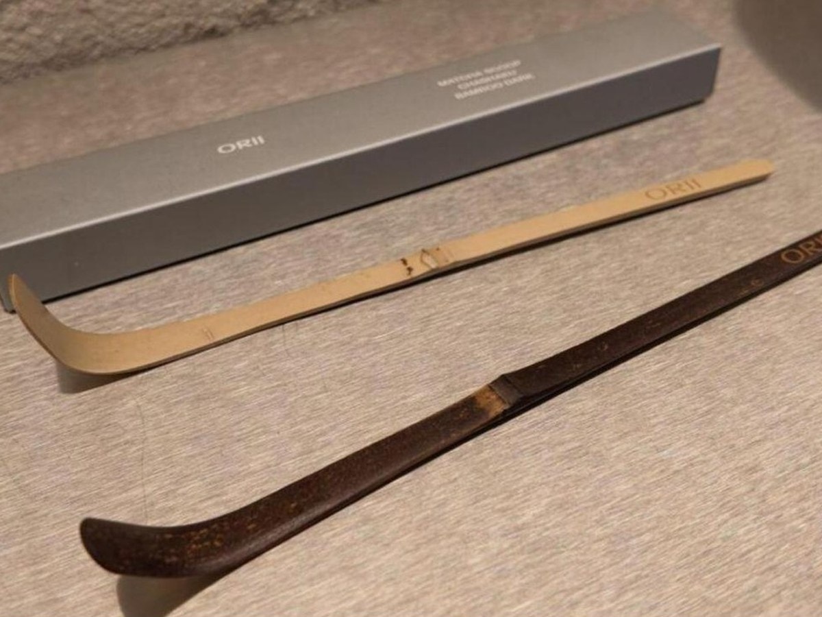 Two bamboo chashaku matcha scoops, one light and one dark, branded with the ORII name, in front of an ORII gift box