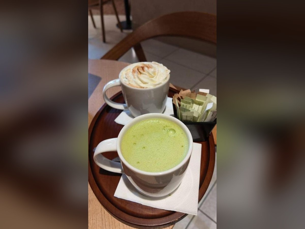 A plain matcha latte in a mug next to a Pumpkin Spice Latte with whipped cream on a wooden tray at Starbucks in Rome
